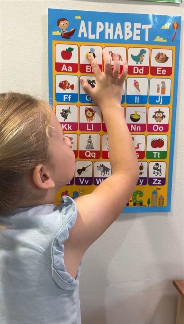 A child reaching up to touch letters on a colourful alphabet poster on the wall