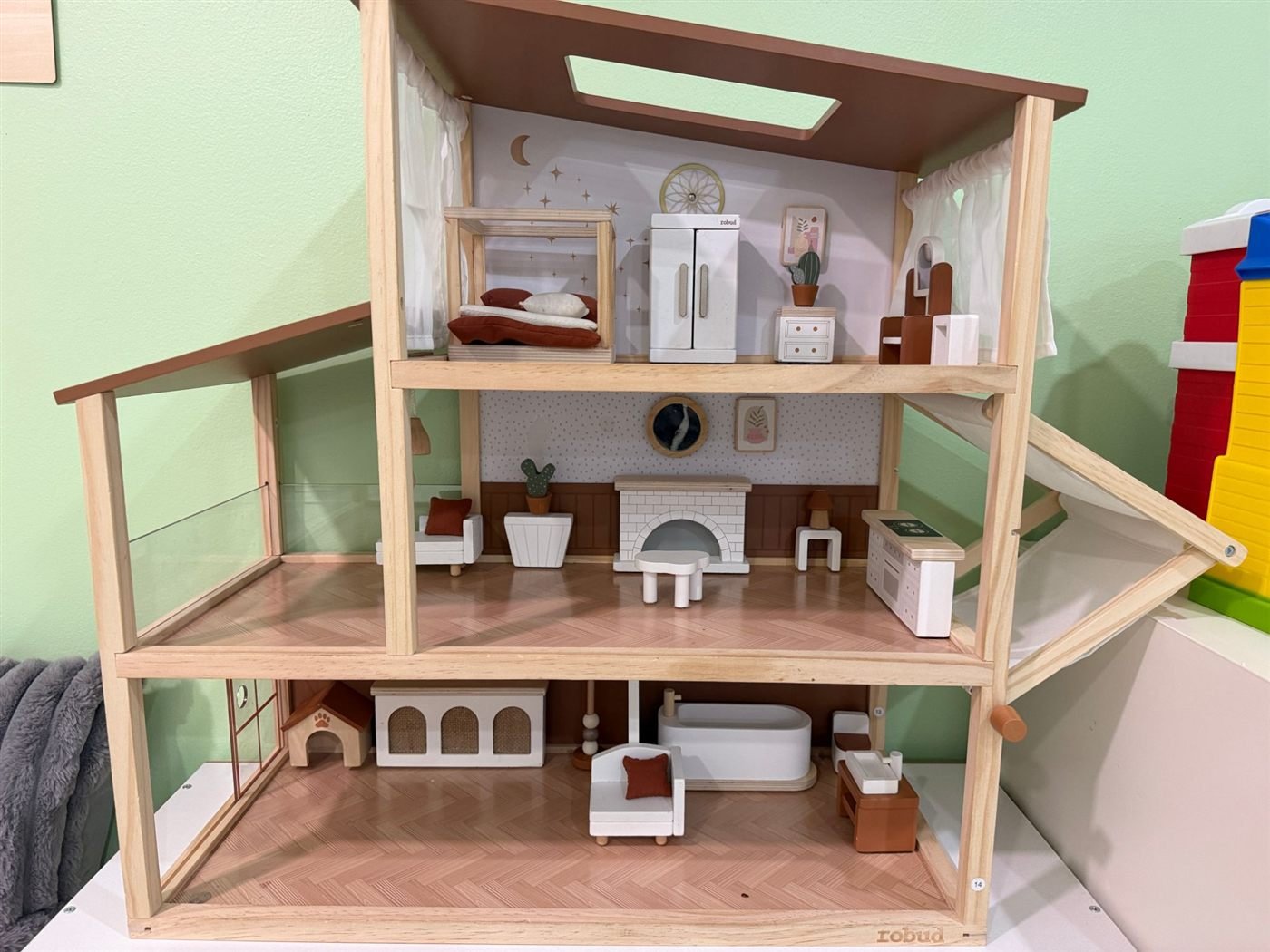 A three-level wooden dollhouse furnished with a bed, fireplace, bathtub and a small dog house