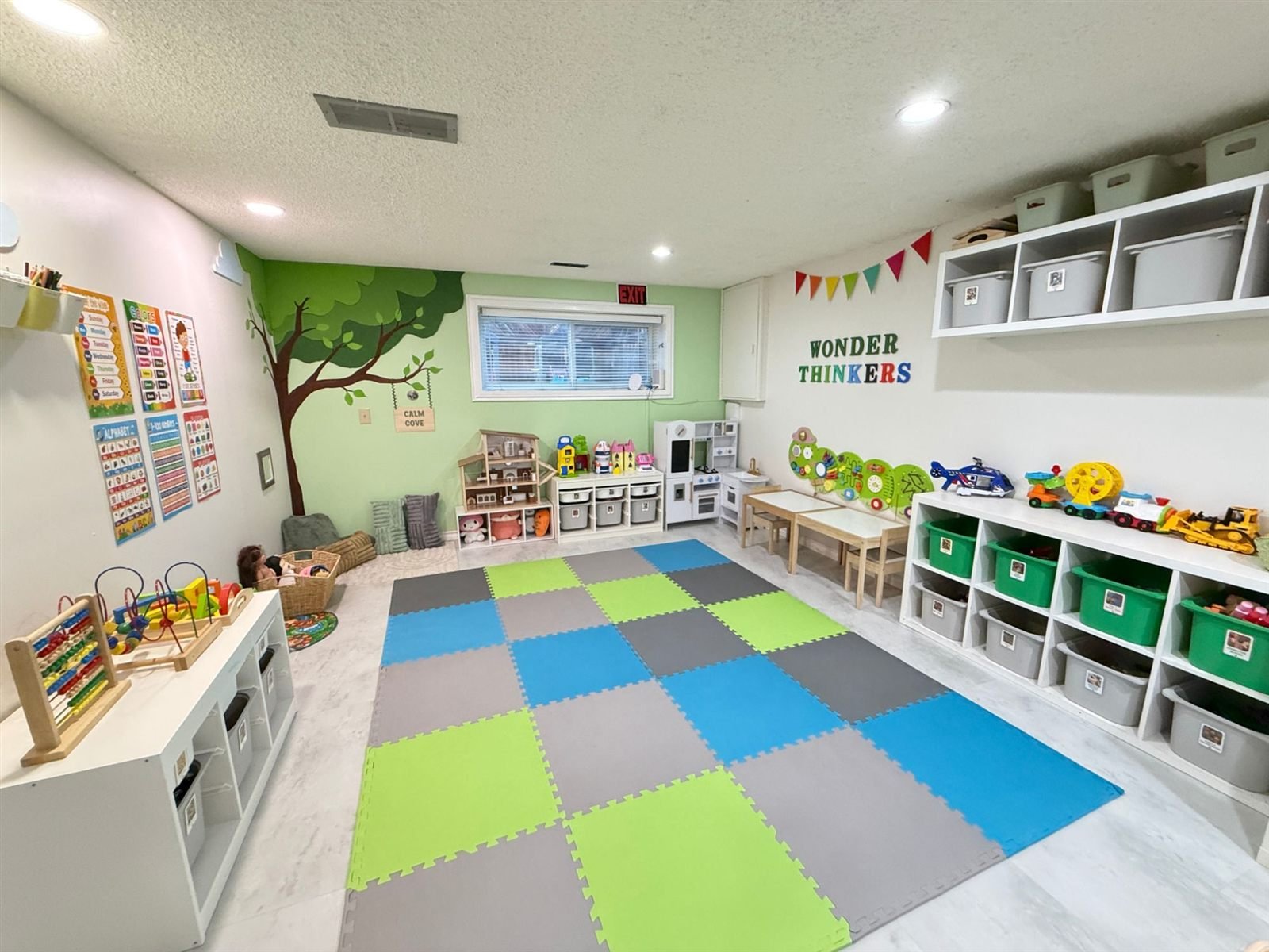 The Wonder Thinkers playroom with a painted tree mural, foam play mat, low toy shelves and learning posters