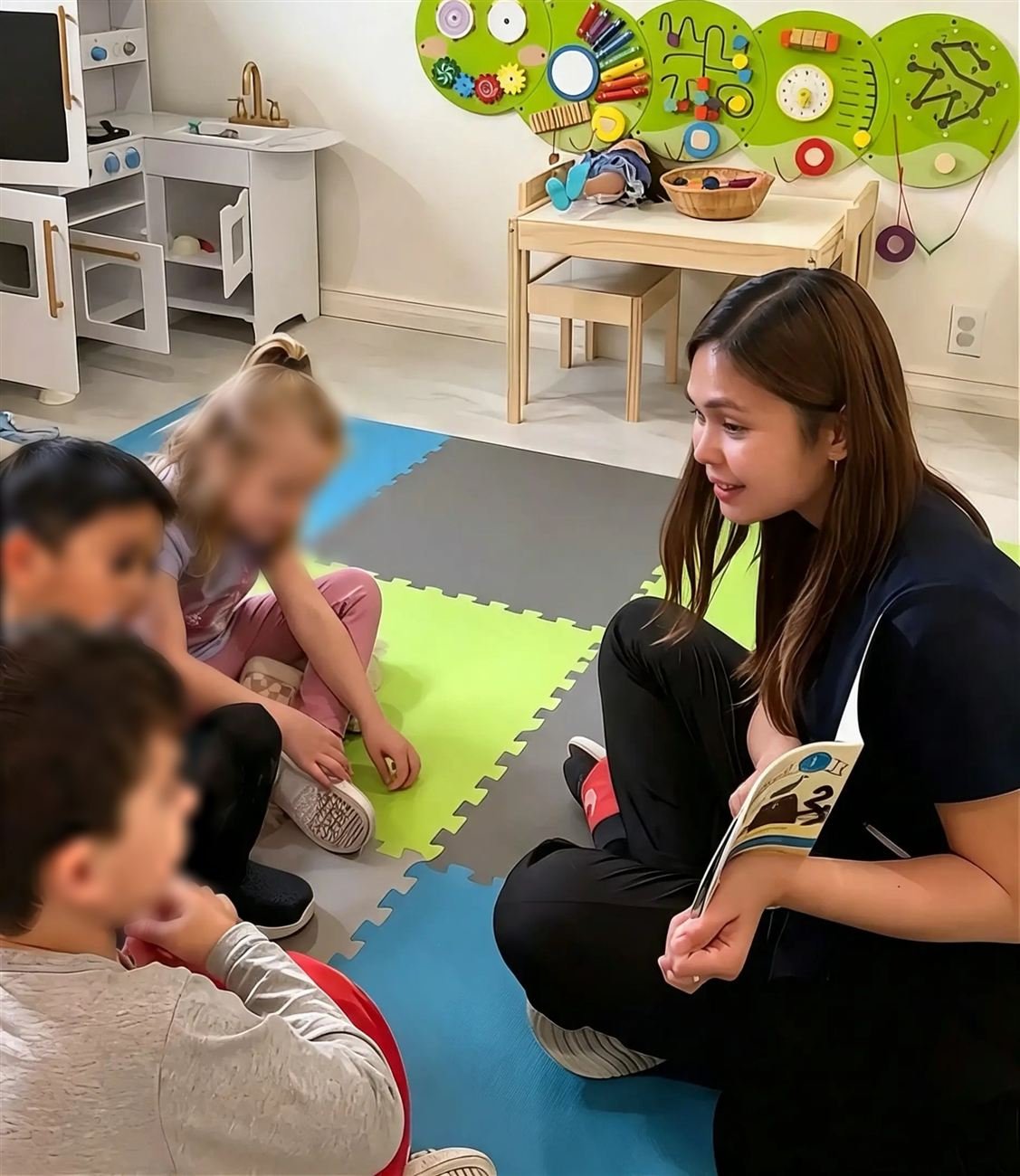 Teacher Marge reading a book with a small group of children gathered around her on the playroom floor
